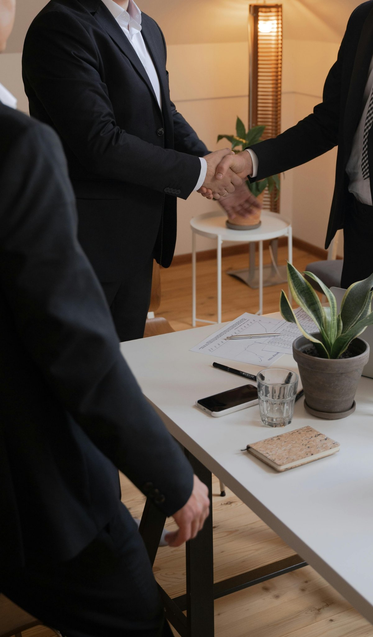 Two people shaking hands over a table with financial documents